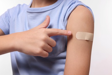 Boy pointing at sticking plaster after vaccination on his arm against white background, closeup