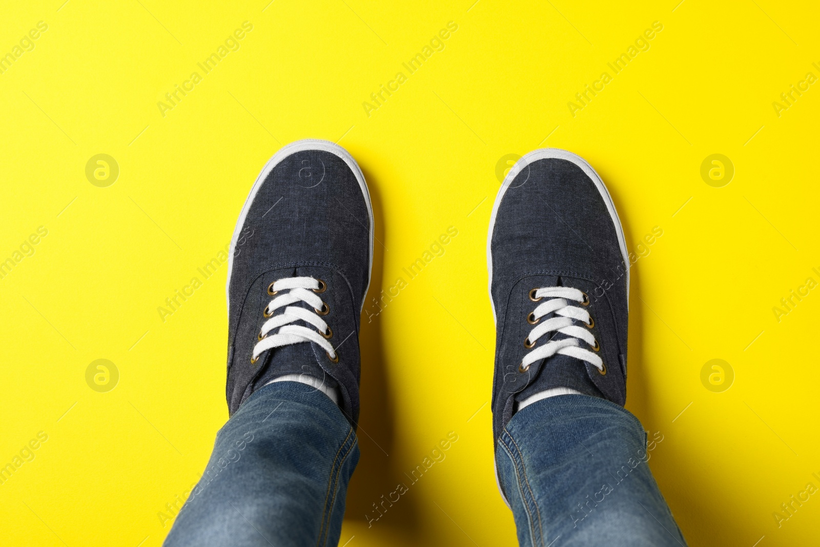 Photo of Child in stylish sneakers standing on yellow background, top view