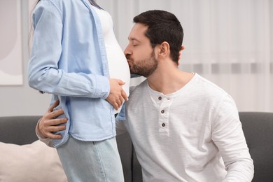Photo of Happy husband kissing pregnant wife's belly at home