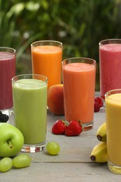 Many different delicious smoothies and ingredients on grey wooden table against blurred background