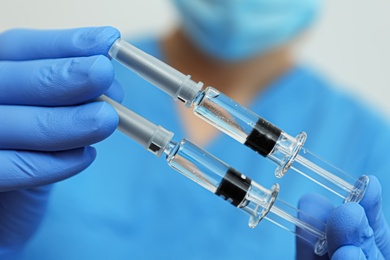 Doctor holding syringes with COVID-19 vaccine, closeup