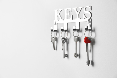 Photo of Metal key holder on light wall indoors. Space for text