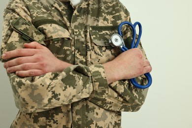 Man in military uniform with crossed arms and stethoscope on light background, closeup. Health care concept