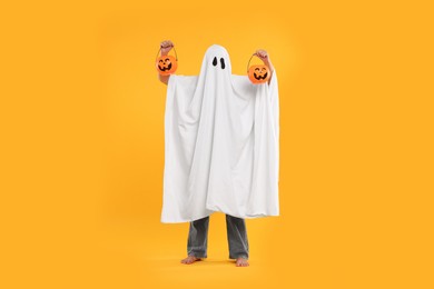 Woman in white ghost costume holding pumpkin buckets on yellow background. Halloween celebration