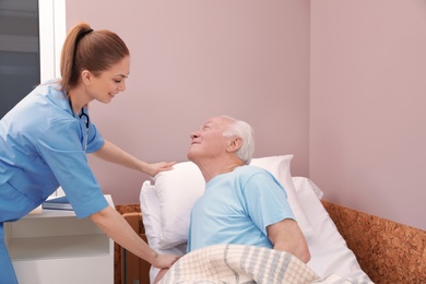 Photo of Nurse assisting senior man on bed in hospital ward