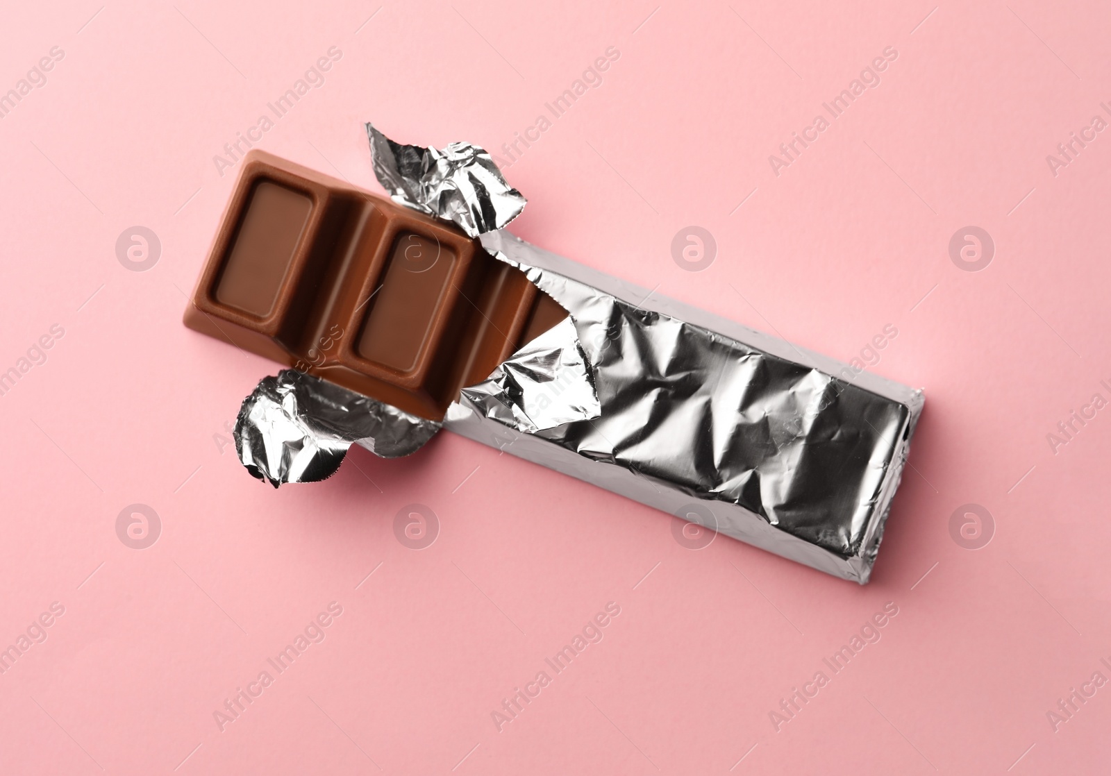 Photo of Delicious chocolate bar wrapped in foil on pink background, top view