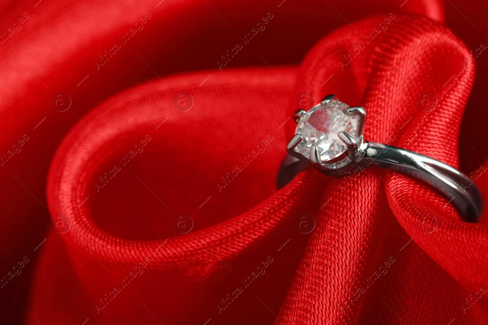 Photo of Beautiful luxury engagement ring with gemstone on red fabric, closeup