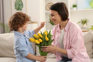 Happy woman with her cute son and bouquet of beautiful flowers at home. Mother's day celebration