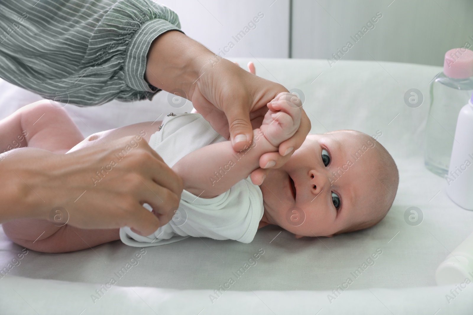 Photo of Mother putting clothes on her little baby at changing table indoors, closeup