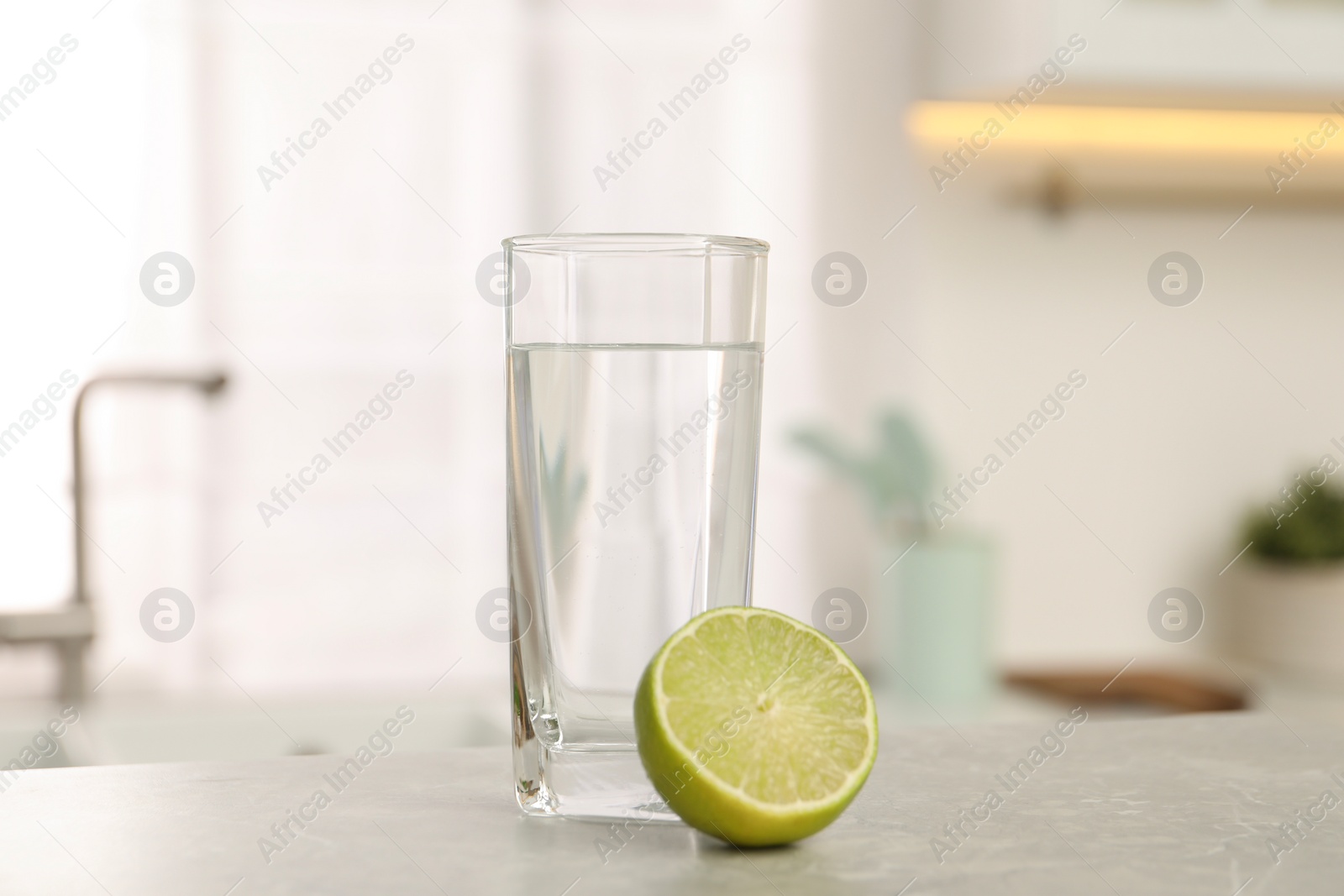 Photo of Filtered water in glass and lime on light table in kitchen, closeup