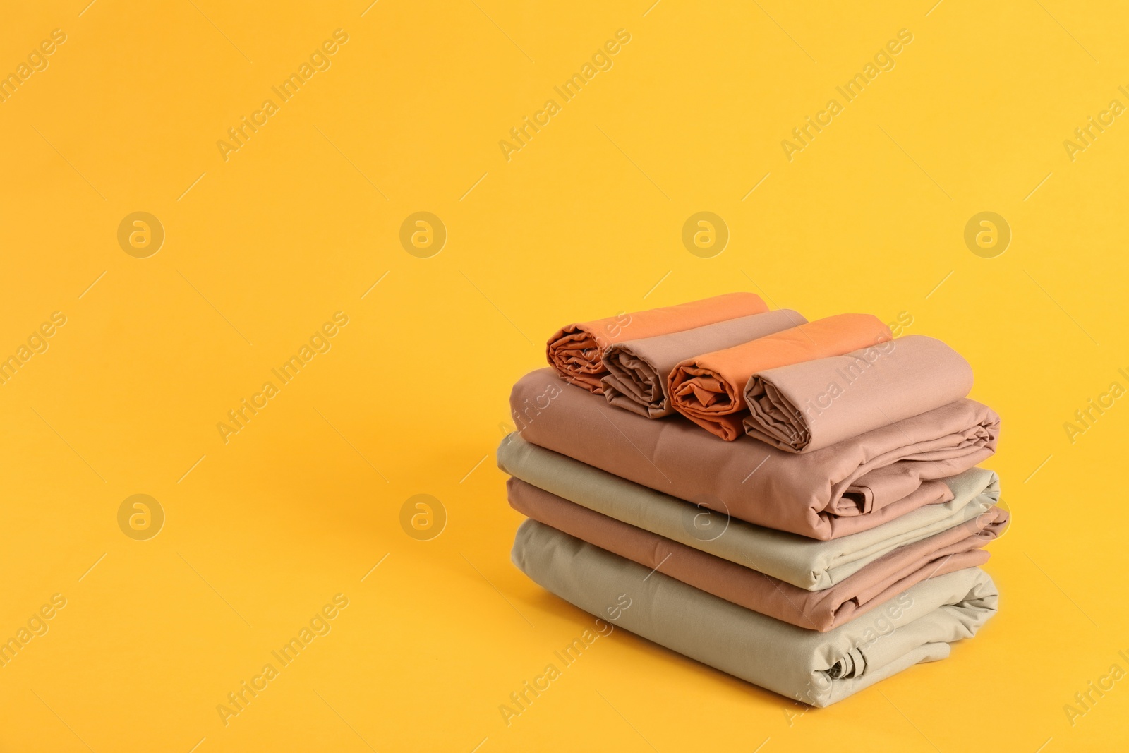 Photo of Stack of clean bed sheets on yellow background. Space for text