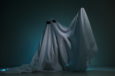 Photo of Creepy ghost. Woman covered with sheet on dark teal background