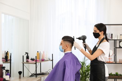 Photo of Professional stylist working with client in salon, space for text. Hairdressing services during Coronavirus quarantine