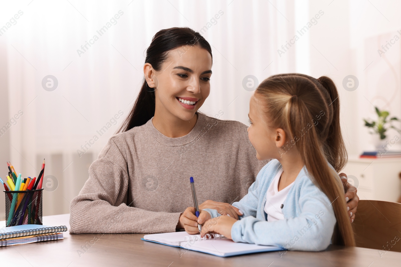 Photo of Dyslexia problem. Mother helping daughter with homework at table in room