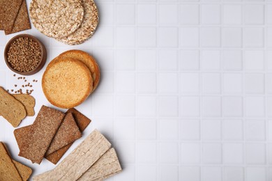 Photo of Rye crispbreads, rice cakes and rusks on white checkered table, flat lay. Space for text