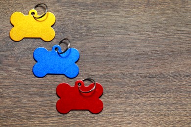 Color metal pet tags in shape of bones with ring on wooden table, flat lay. Space for text