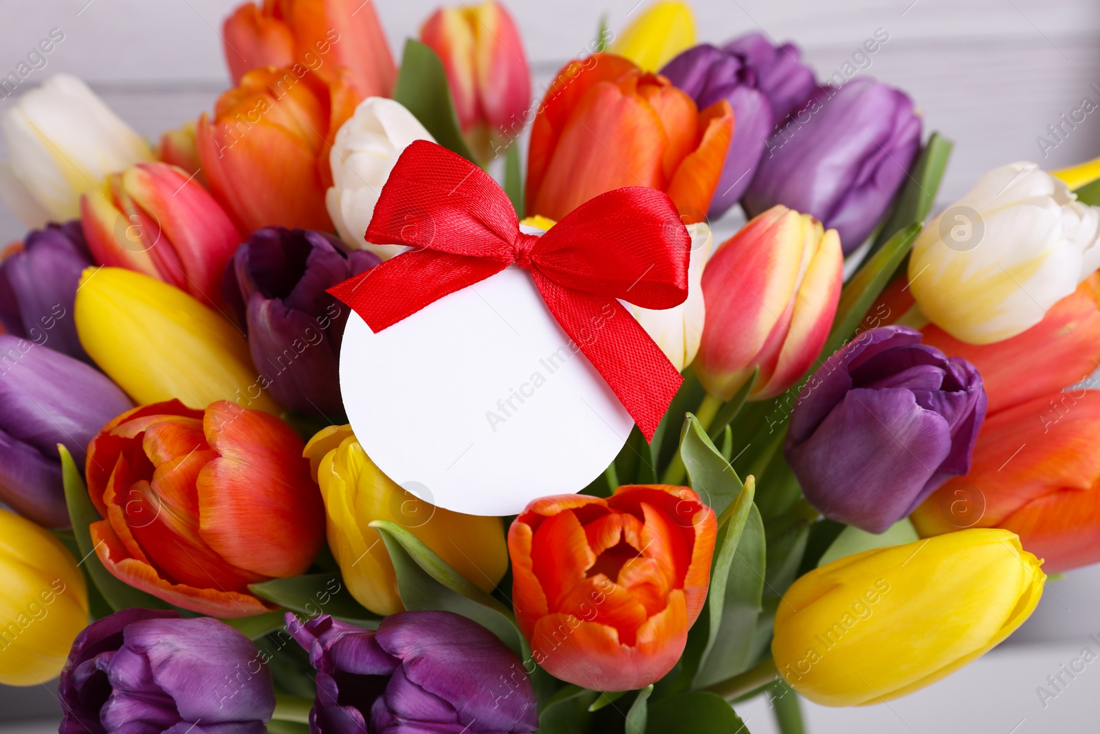 Photo of Bouquet of beautiful colorful tulips with blank card on white wooden background, closeup. Birthday celebration