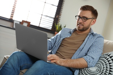 Photo of Young man using laptop in living room