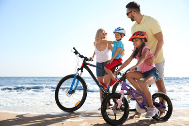 Photo of Happy parents teaching children to ride bicycles on sandy beach near sea