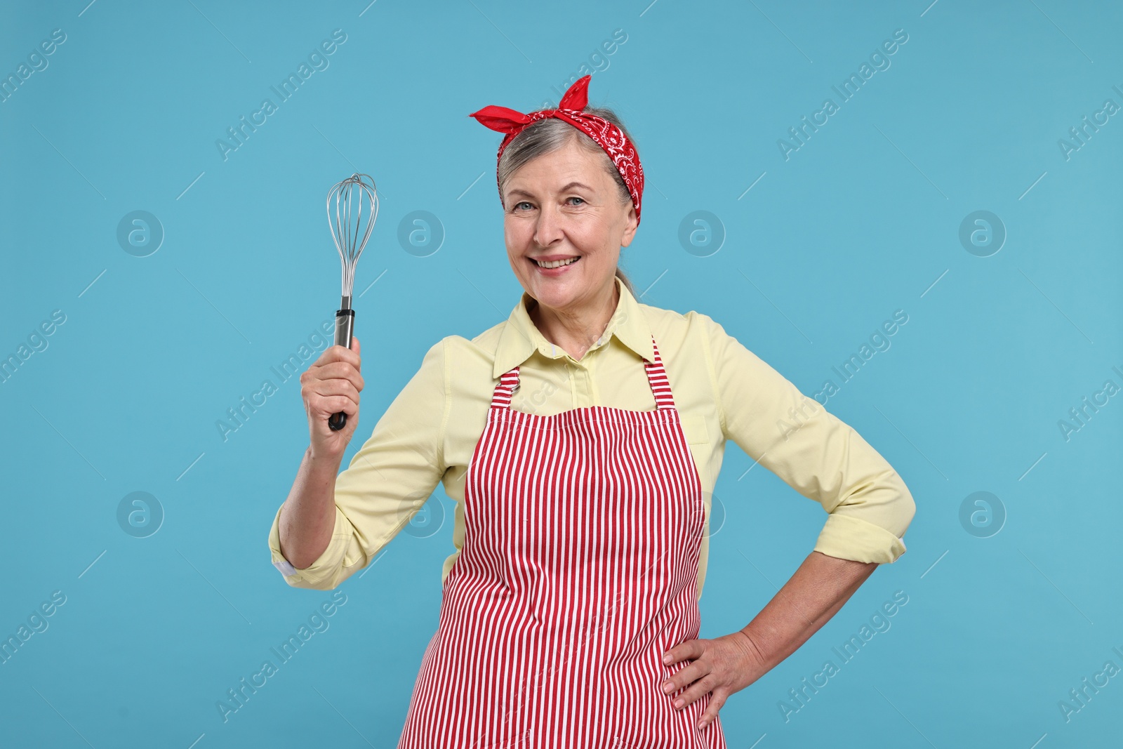 Photo of Happy housewife with whisk on light blue background