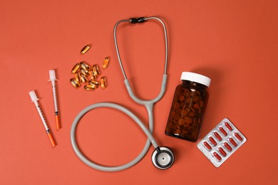 Stethoscope, syringes and pills on crimson background, flat lay. Medical tools