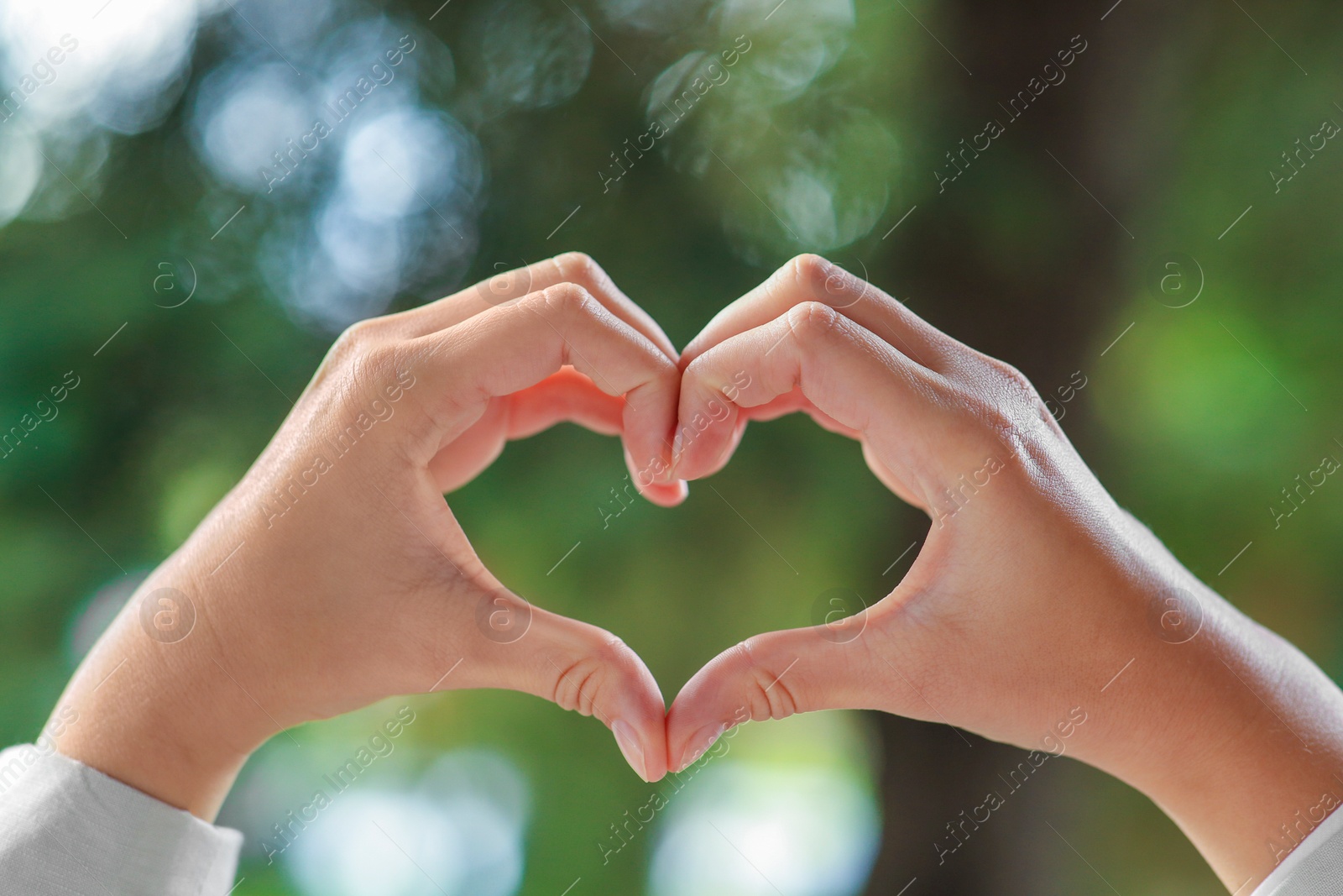 Photo of Woman showing heart gesture with hands against blurred background, closeup. Love concept