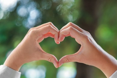 Photo of Woman showing heart gesture with hands against blurred background, closeup. Love concept