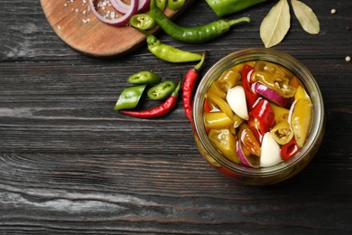 Glass jar with pickled peppers on wooden table, flat lay. Space for text