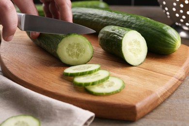 Photo of Woman cutting cucumber on wooden board at table, closeup