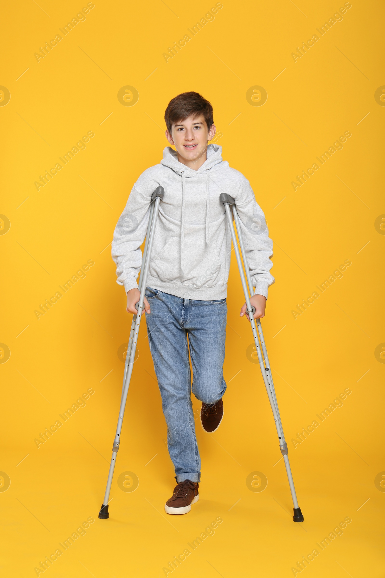 Photo of Teenage boy with injured leg using crutches on yellow background