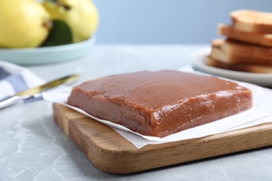 Photo of Wooden board with fresh quince paste on light grey table, closeup