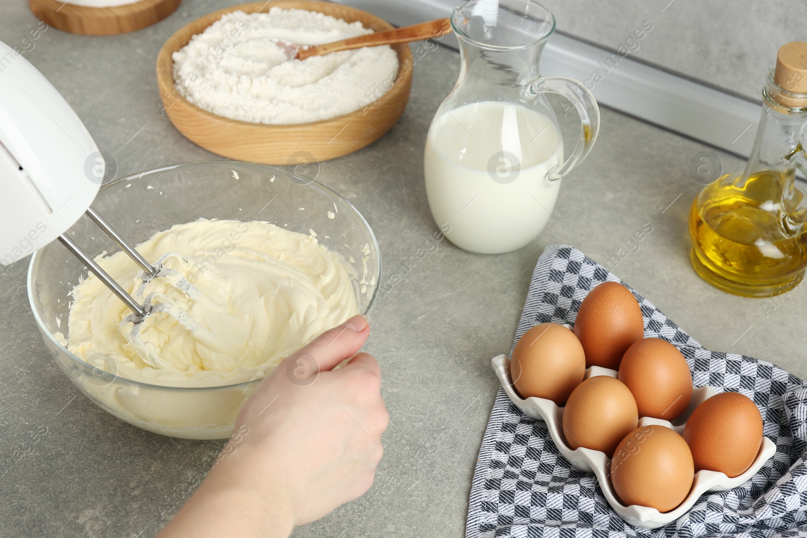 Photo of Woman whipping white cream with mixer at light grey table, closeup