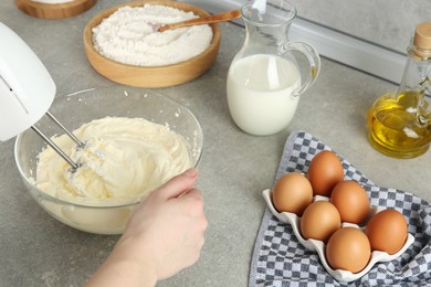 Photo of Woman whipping white cream with mixer at light grey table, closeup
