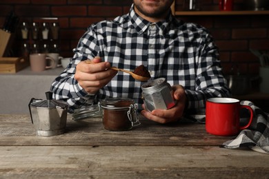 Photo of Man putting ground coffee into moka pot at wooden table in kitchen, closeup