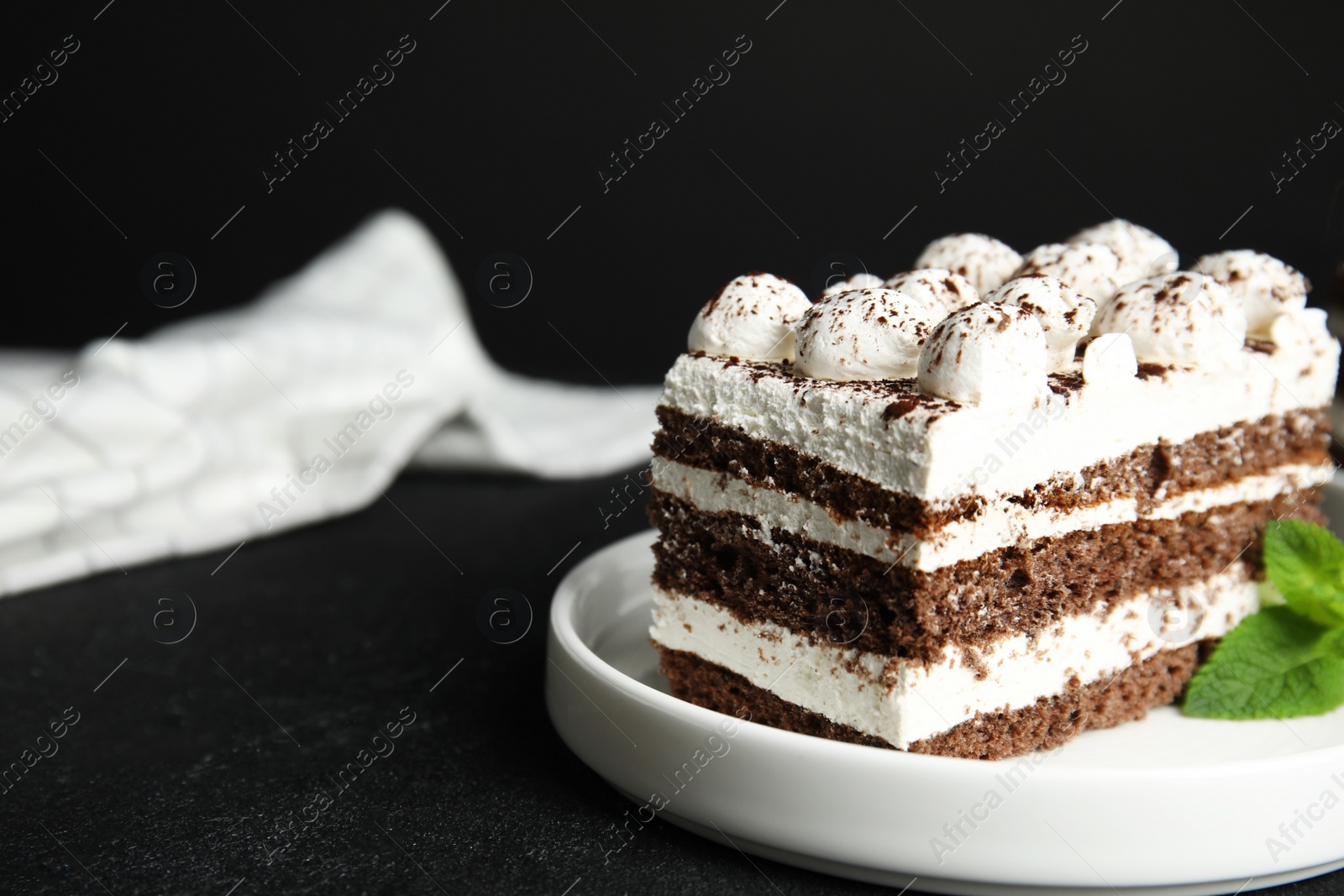 Photo of Tiramisu cake with mint on table against dark background, closeup. Space for text