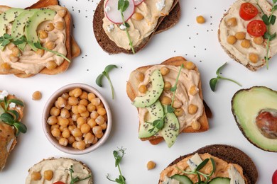 Photo of Delicious sandwiches with hummus and different ingredients on white background, flat lay