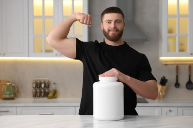 Photo of Young man with jar of protein powder at white marble table in kitchen