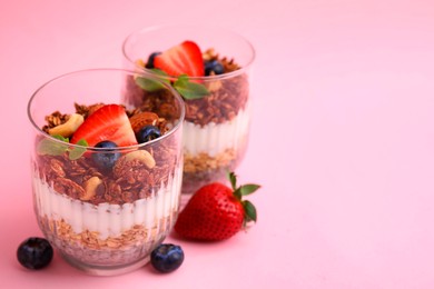 Photo of Tasty granola with berries, nuts, yogurt and chia seeds in glasses on pink background, space for text