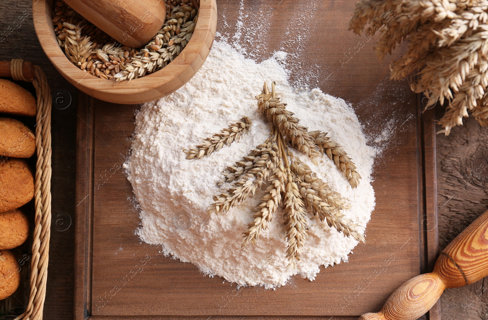 Photo of Pile of wheat flour and spikes on wooden table, flat lay