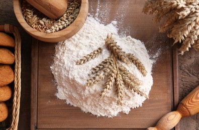 Photo of Pile of wheat flour and spikes on wooden table, flat lay