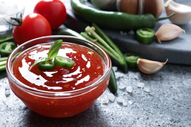 Photo of Spicy chili sauce in glass bowl on grey table, space for text