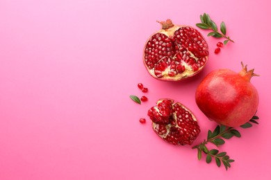 Photo of Fresh pomegranates and green leaves on pink background, flat lay. Space for text