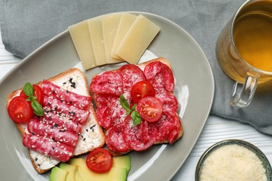 Photo of Tasty toasts with slices of sausages, tomatoes and cheese on white wooden table, flat lay