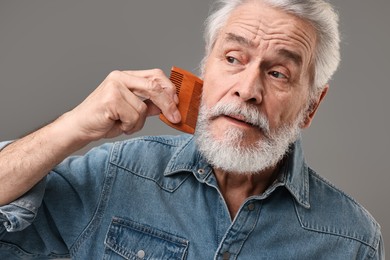 Senior man combing beard on grey background