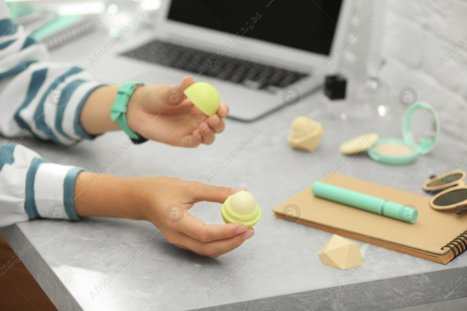 Photo of Young beauty blogger with lip balm at light grey marble table, closeup