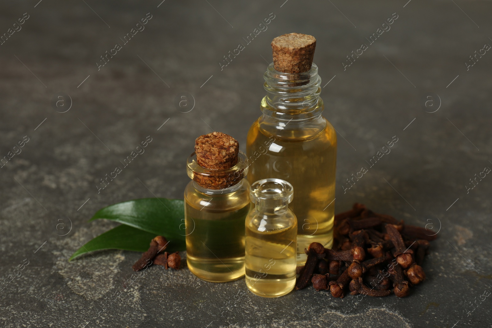 Photo of Essential oil, dried cloves and green leaves on grey table