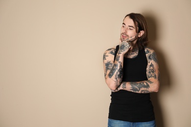 Photo of Young man with tattoos on body against beige background. Space for text