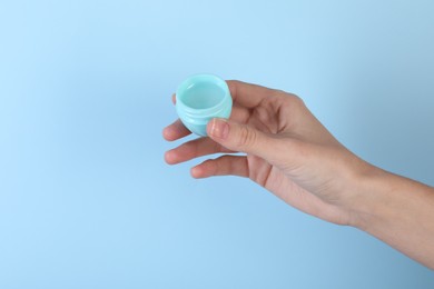 Woman with lip balm on light blue background, closeup