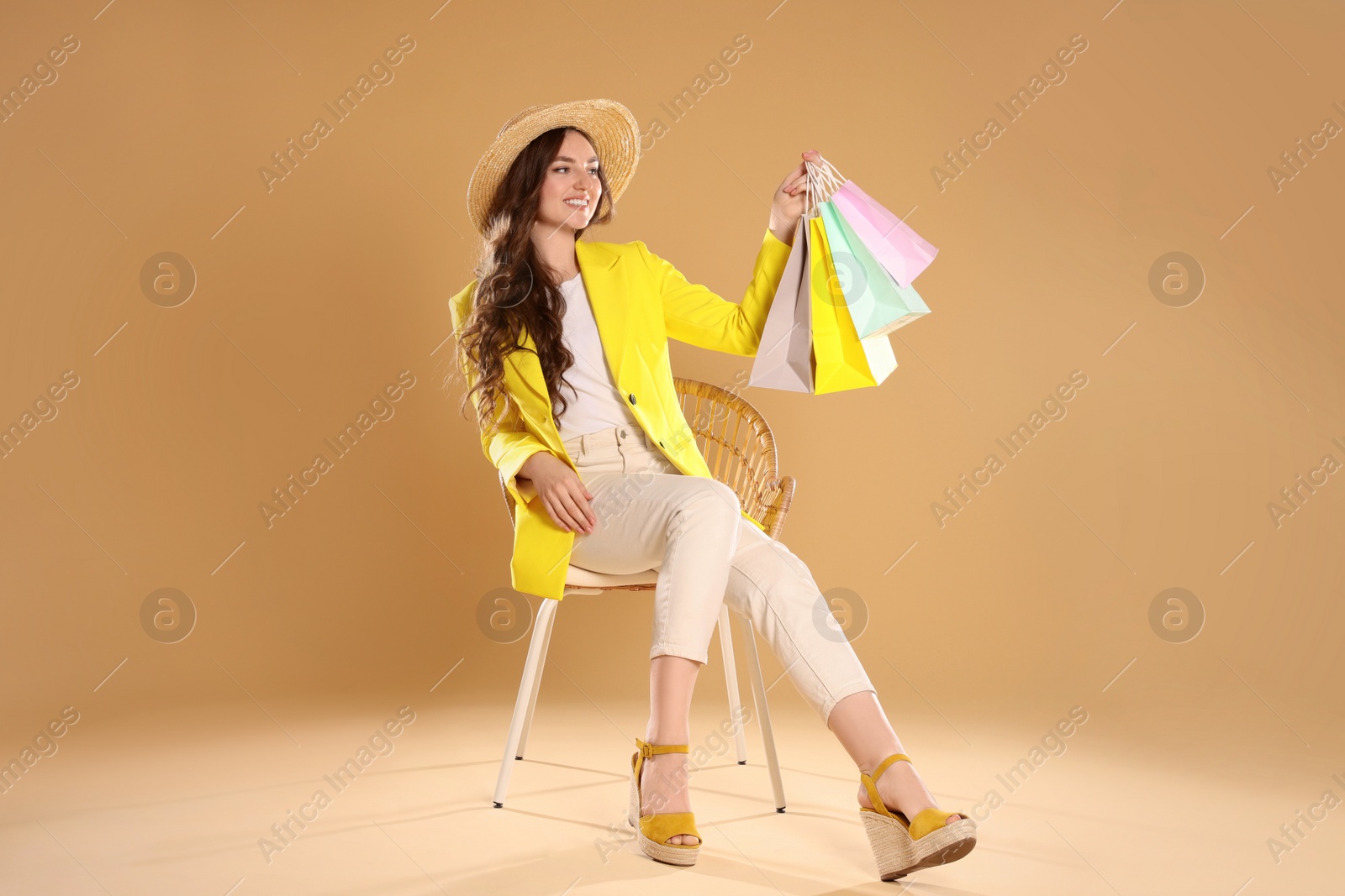 Photo of Happy woman holding many colorful shopping bags on armchair against beige background