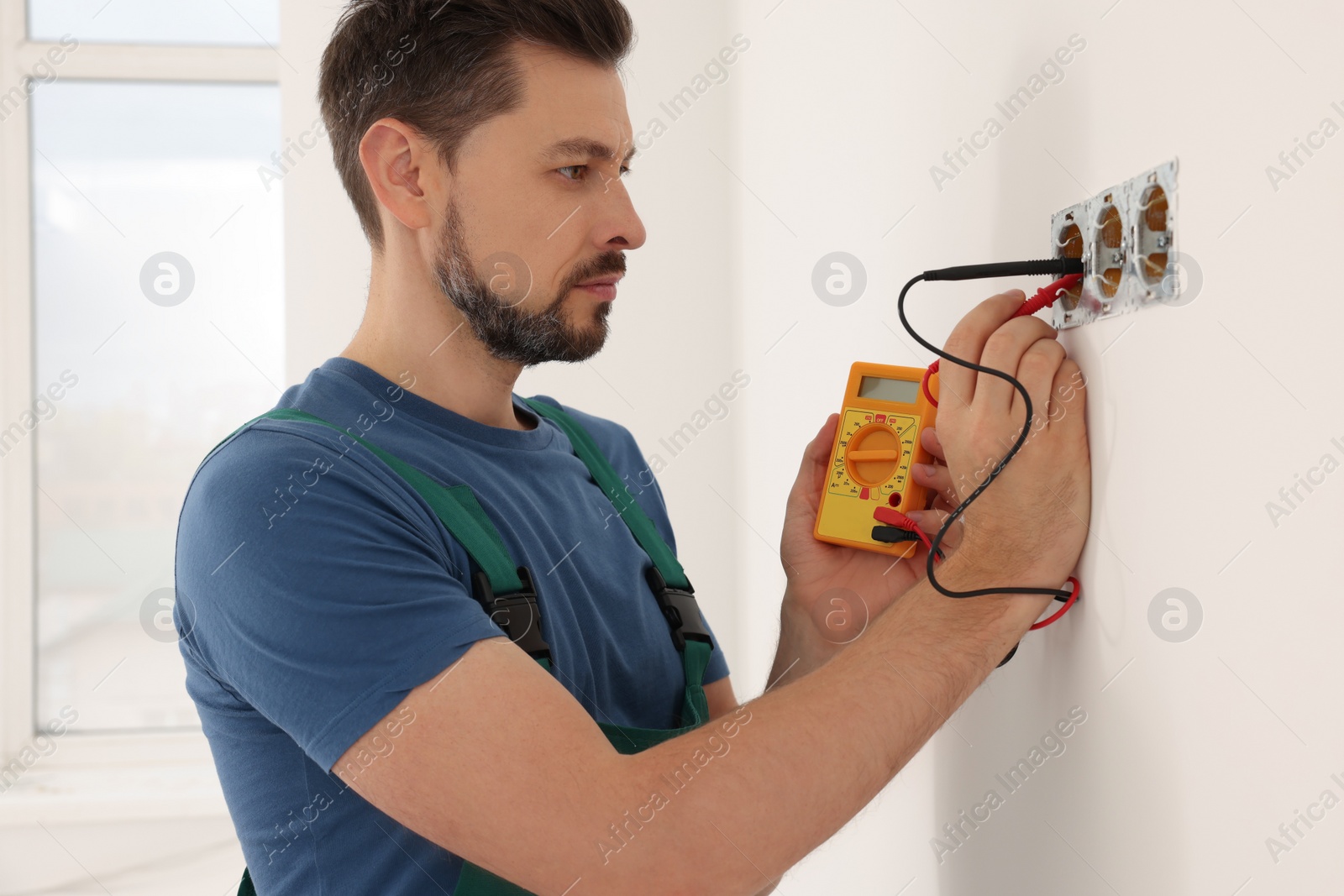 Photo of Electrician in uniform with tester checking voltage indoors